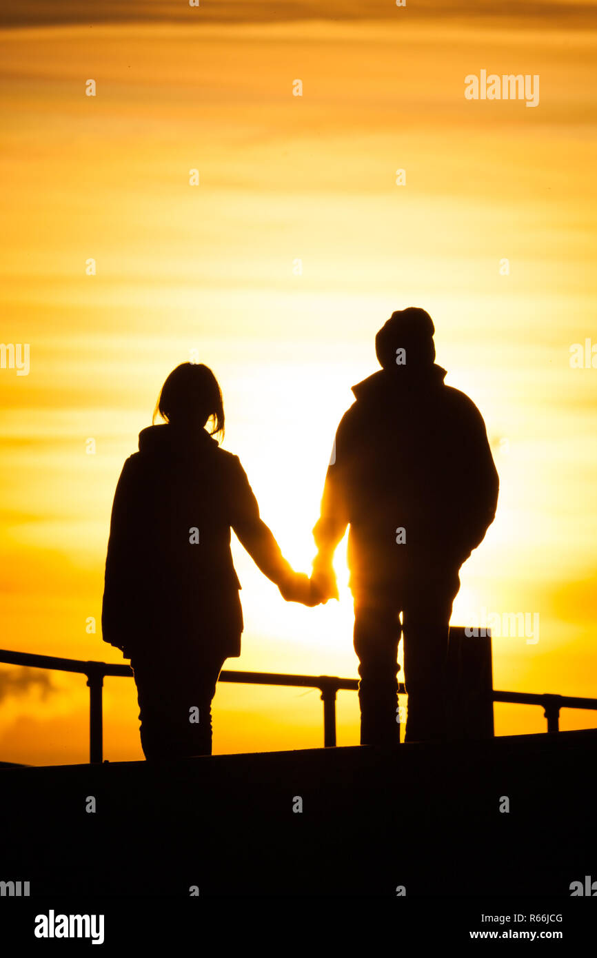 Una coppia (uomo e donna) in vi tardo 20s, inizio 30s tenendo le mani mentre si cammina durante il tramonto lungo la passeggiata a Southsea, Regno Unito Foto Stock