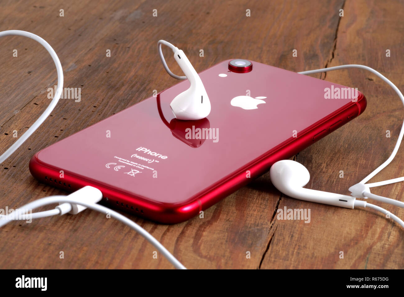 Koszalin, Polonia - Dicembre 04, 2018: Rosso iPhone XR su un tavolo di legno con gli auricolari bianchi. L'iPhone XR è smart phone con multi touch screen produ Foto Stock