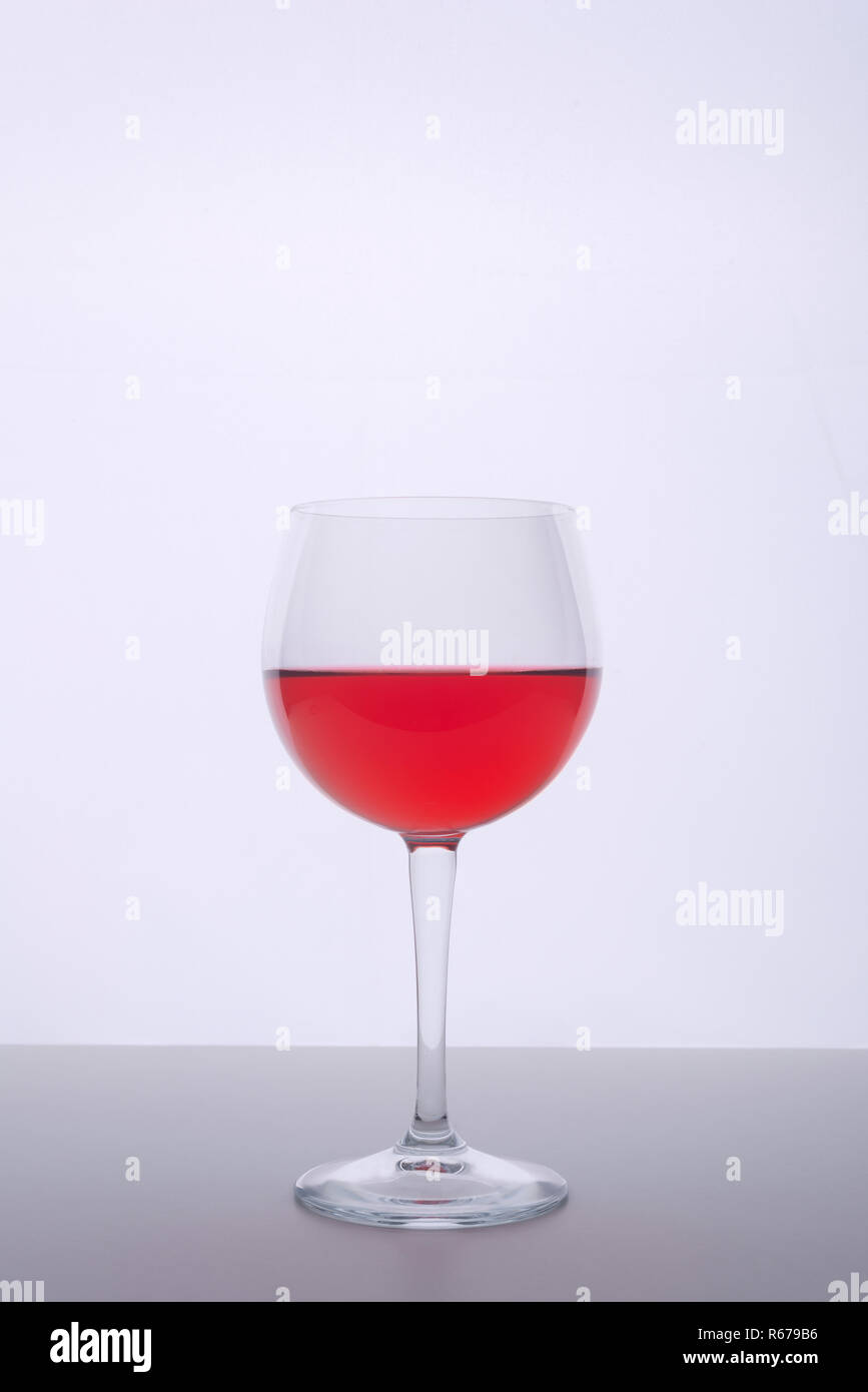 Un bicchiere con un drink rosso su una superficie bianca Foto Stock