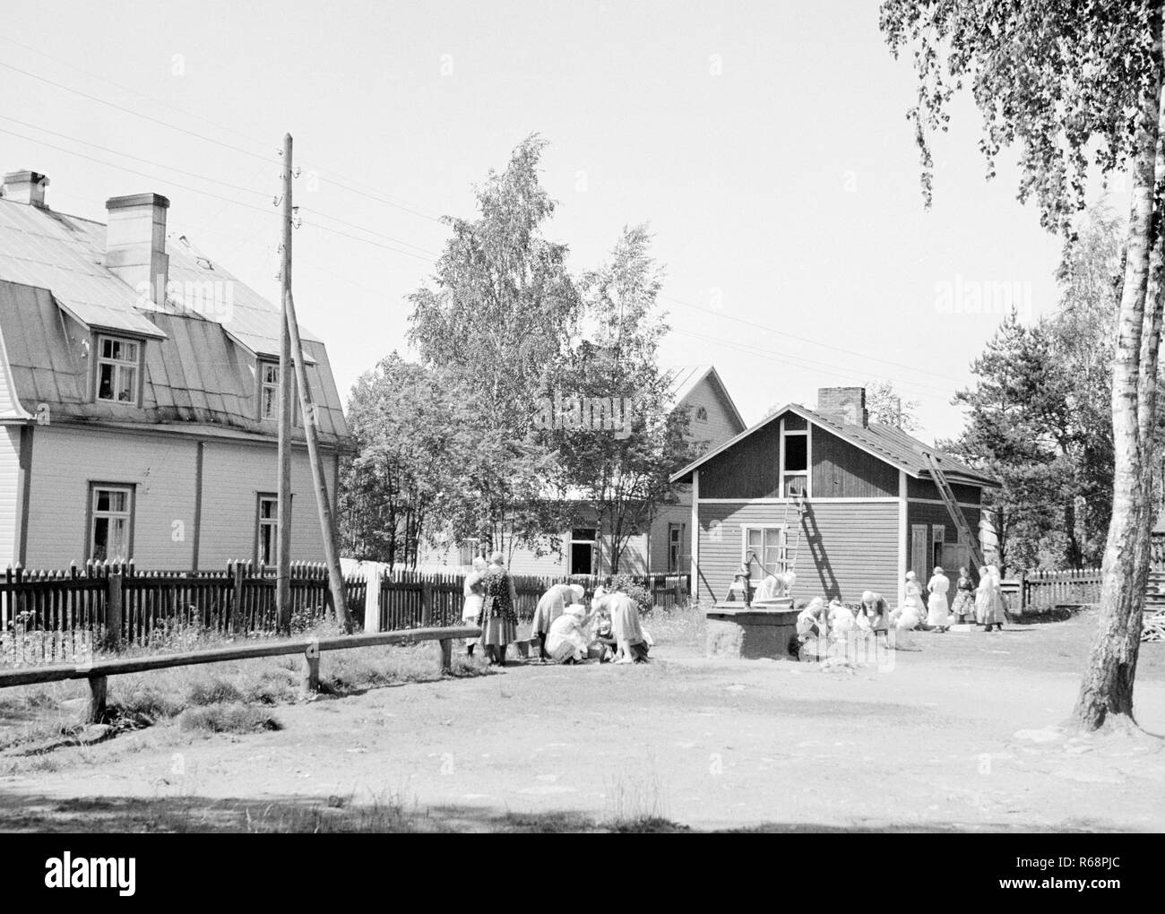 Street View di area rurale con case in legno con le donne a lavare i panni attorno a un pozzo 1920s-1930s, Finlandia Foto Stock