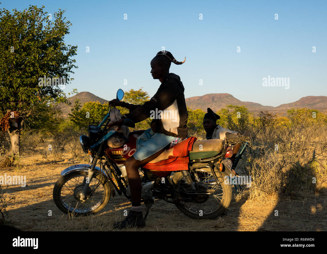 Himba tribe uomo con la tradizionale acconciatura sul suo motociclo, Provincia del Cunene, Oncocua, Angola Foto Stock