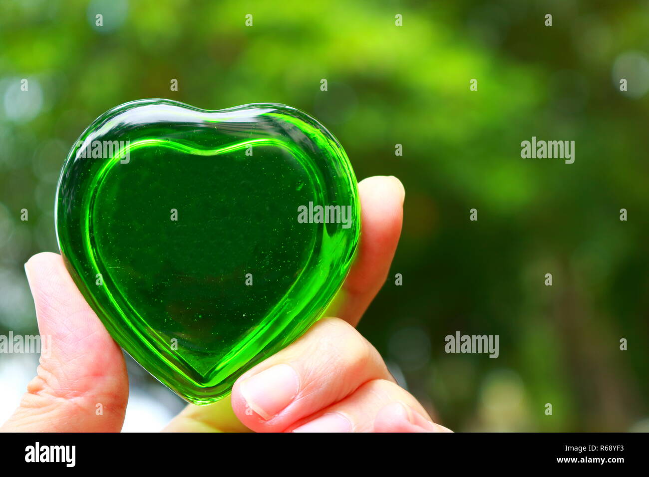 Vista dettagliata del cuore verde realizzata in vetro in una mano Foto Stock