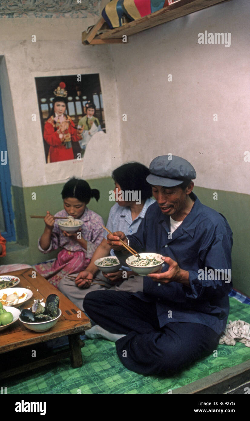 Cina settentrionale 1980 Comune in provincia Waoning in un interno di una casa in cui una famiglia sono di mangiare un pasto seduti su un kang un letto stufa che è una piattaforma di mattoni dove incanalata aria viene alimentata da un incendio fornendo calore, solitamente a fuoco di legno. Foto Stock