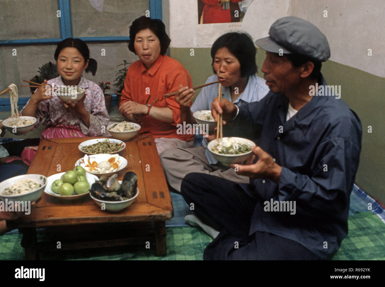 Cina settentrionale 1980 Comune in provincia Waoning in un interno di una casa in cui una famiglia sono di mangiare un pasto seduti su un kang un letto stufa che è una piattaforma di mattoni dove incanalata aria viene alimentata da un incendio fornendo calore, solitamente a fuoco di legno. Foto Stock