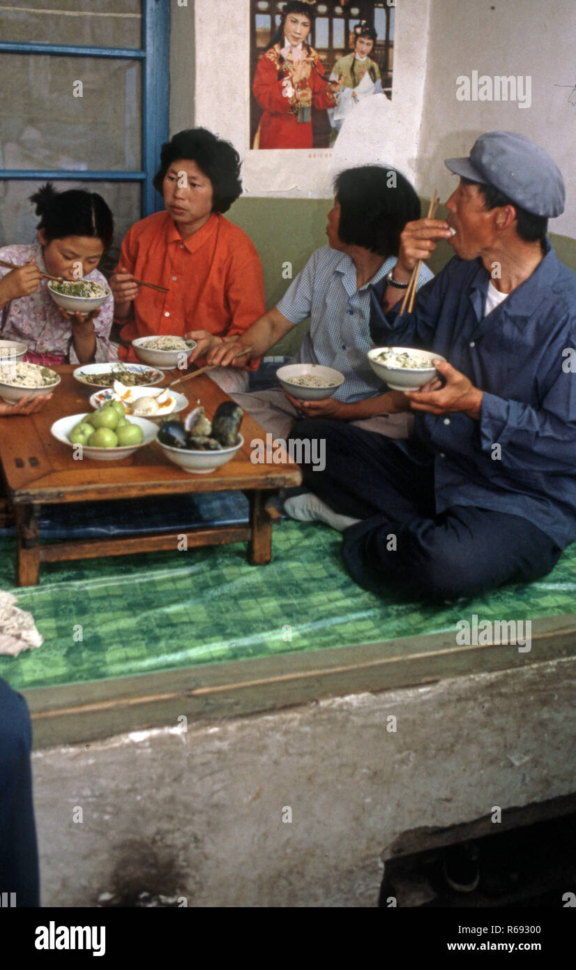 Cina settentrionale 1980 Comune in provincia Waoning in un interno di una casa in cui una famiglia sono di mangiare un pasto seduti su un kang un letto stufa che è una piattaforma di mattoni dove incanalata aria viene alimentata da un incendio fornendo calore, solitamente a fuoco di legno. Foto Stock