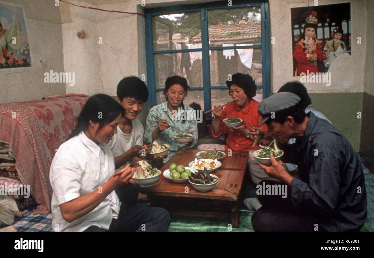 Cina settentrionale 1980 Comune in provincia Waoning in un interno di una casa in cui una famiglia sono di mangiare un pasto seduti su un kang un letto stufa che è una piattaforma di mattoni dove incanalata aria viene alimentata da un incendio fornendo calore, solitamente a fuoco di legno. Foto Stock