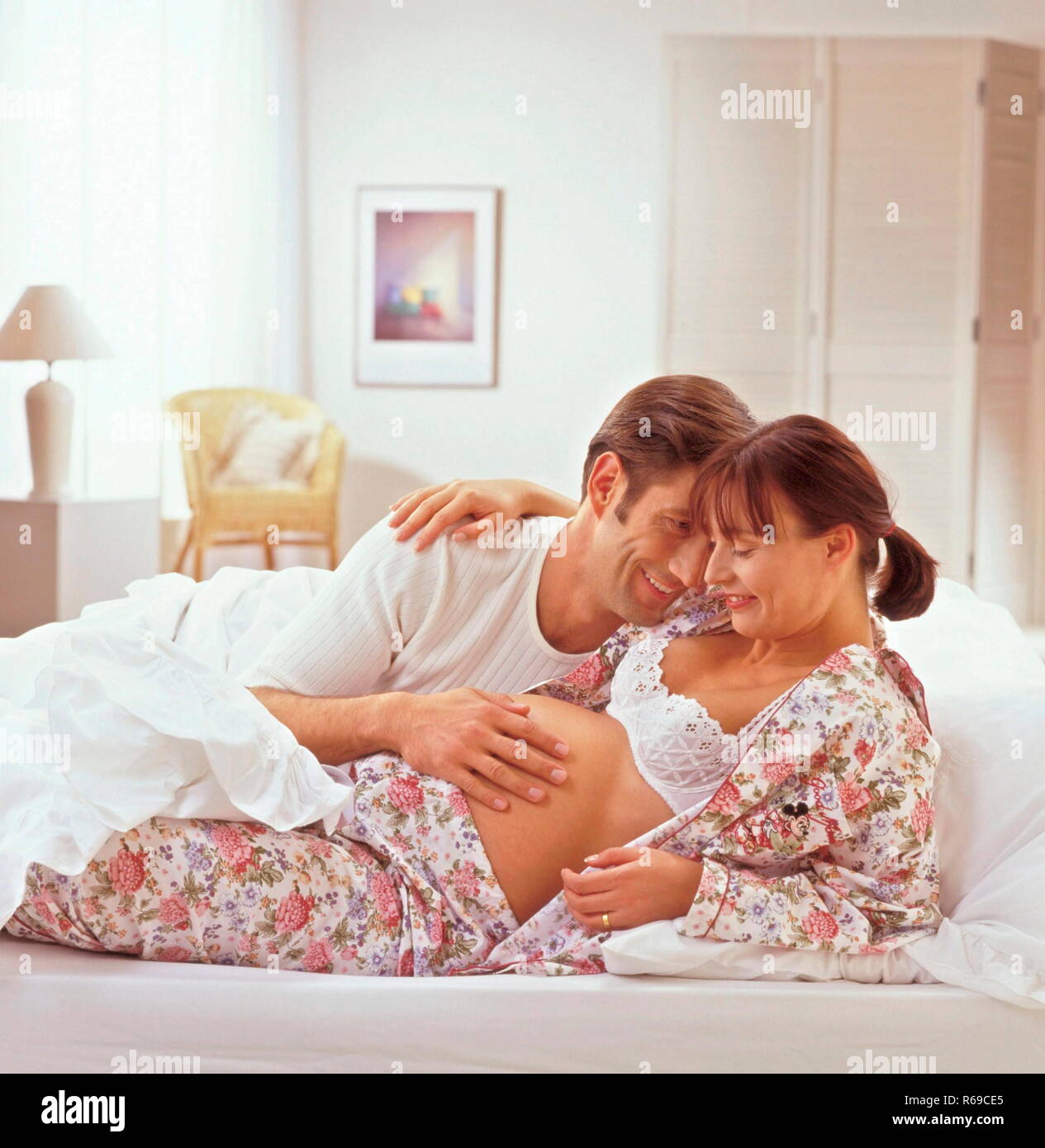 Ritratto, Mann liegt mit circuizione hochschwangeren Frau auf dem Bett und beruehrt ihren Bauch Foto Stock