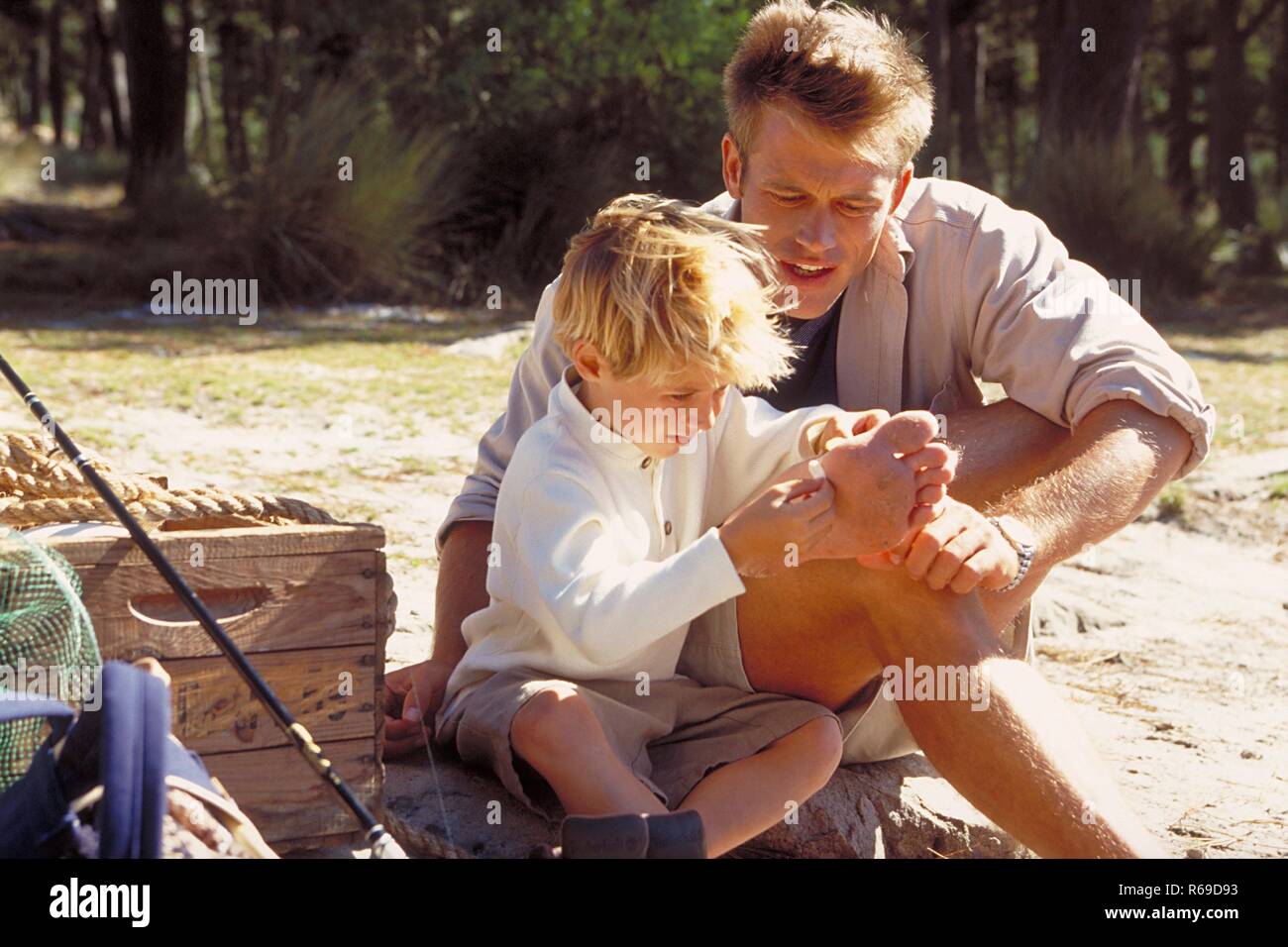 All'aperto, 6 Jahre alter blondr Junge hilft seinem Vater im Wald einen Stachel aus seinem Fuss zu entfernen Foto Stock