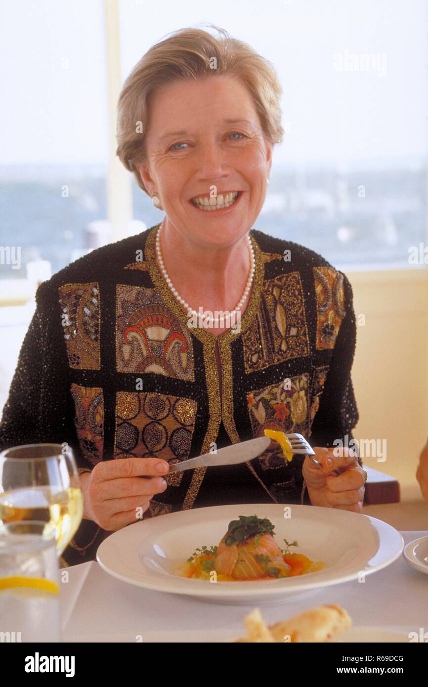 Ritratto, Innenraum, blonde Frau, ca. 65 Jahre alt, im Restaurant bei einem Glas Weisswein und einer Lachspastete Foto Stock