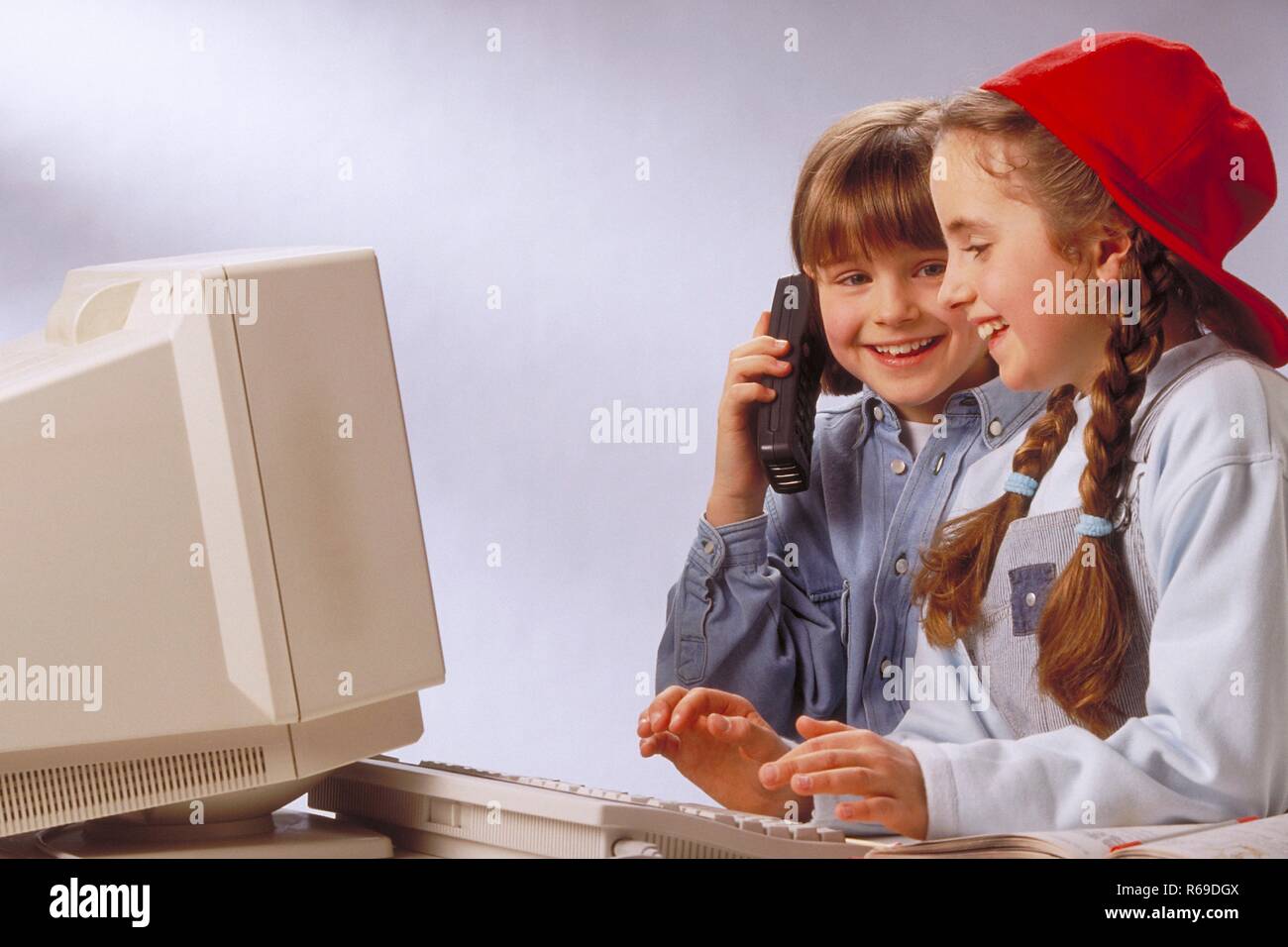 Ritratto, Innenraum, 2 10-11 jaehrige Maedchen sitzen am Computer und telefonieren Mit einem a portata di mano Foto Stock