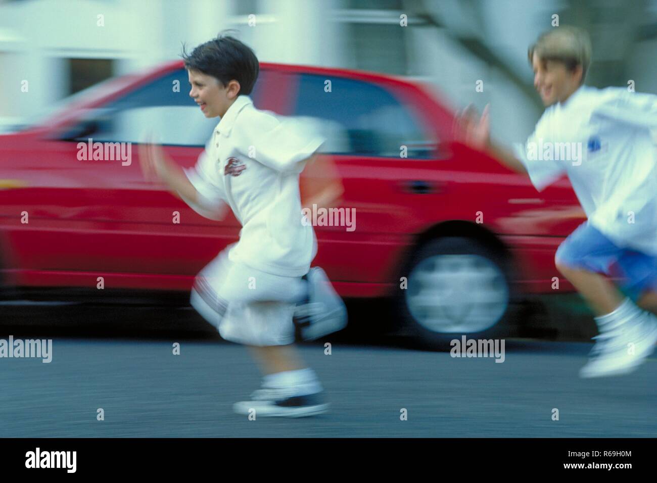 Ritratto, Ganzfigur, zwei 7-8 Jahre alte Jungen bekleidet mit weissen T-Shirts und Shorts laufen un einem roten Auto vorbei die Strasse entlang Foto Stock