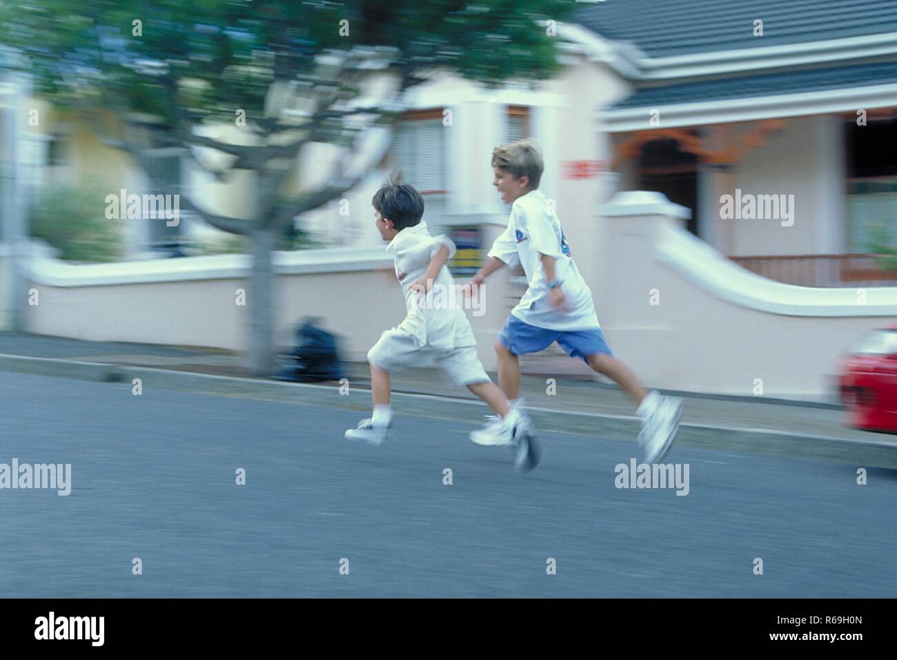 Ritratto, Ganzfigur, zwei 7-8 Jahre alte Jungen bekleidet mit weissen T-Shirts und Shorts laufen un einem Haus vorbei die Strasse entlang Foto Stock