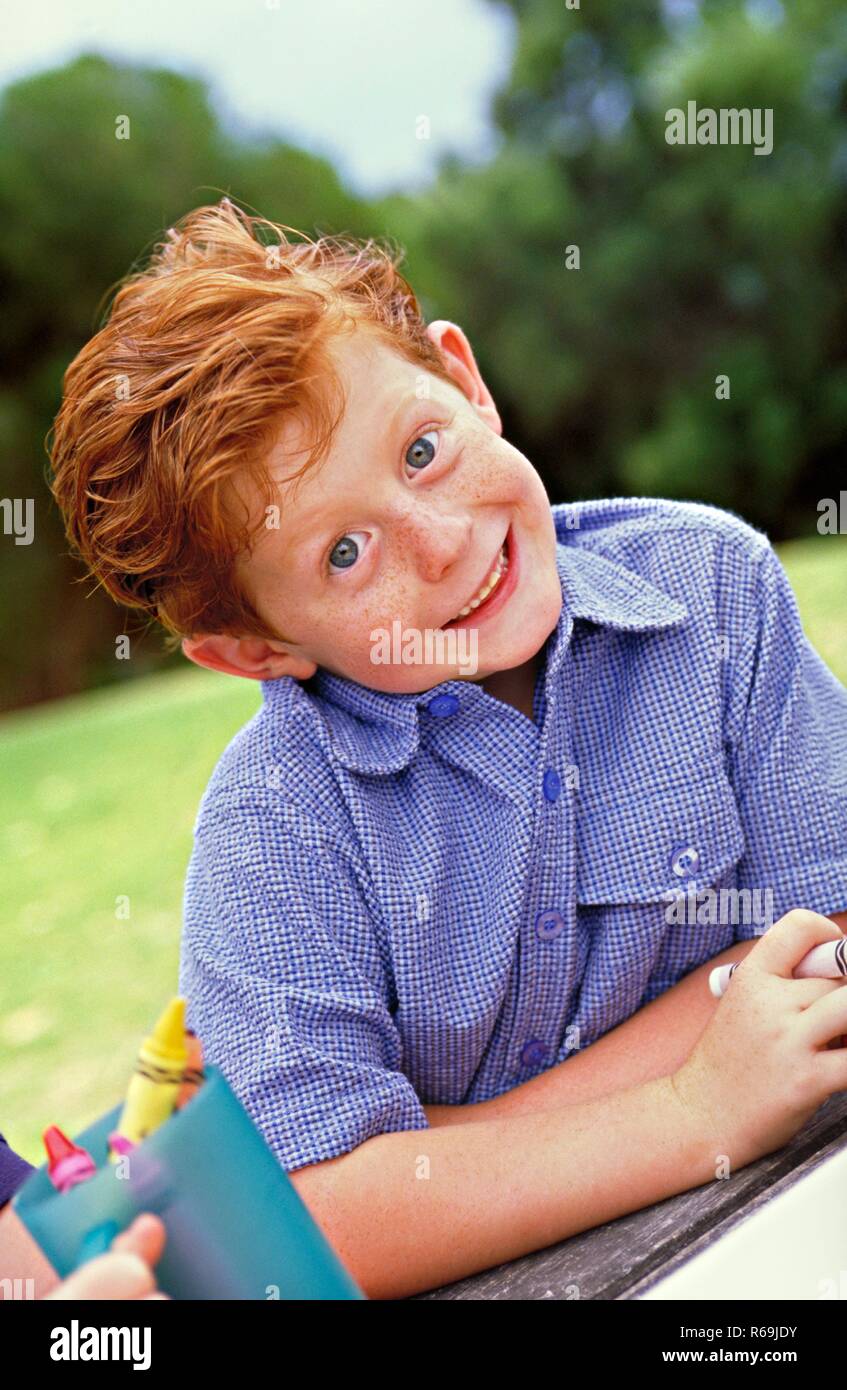 Ritratto, rothaariger Junge mit Sommersprossen und groen blauen Augen, 7  Jahre, bekleidet mit blauem Hemd auf einer Wiese im Garten, haelt einen  dito Vor den Mund Foto stock - Alamy