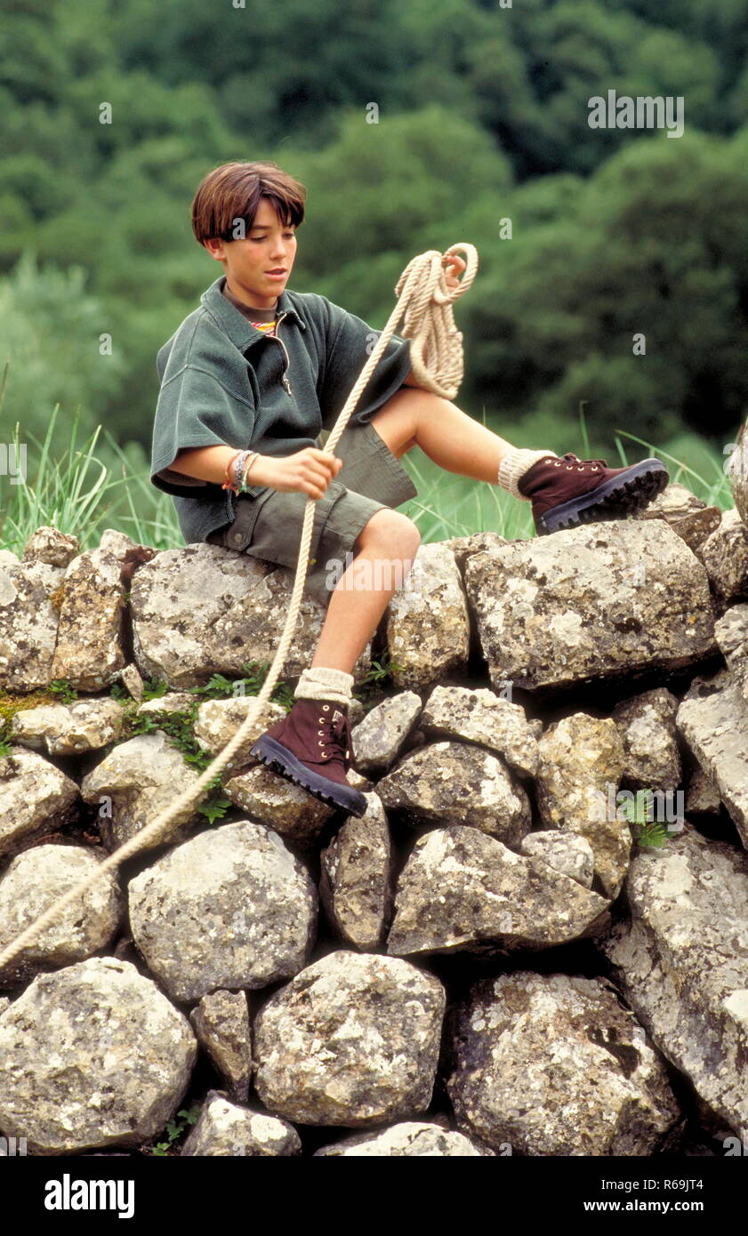 Ritratto, Junge mt braunen Haaren, 14 Jahre, bekleidet mit shorts cachi und Hemd und Wanderschuhen Seil mit beim Klettern in Felsen Foto Stock