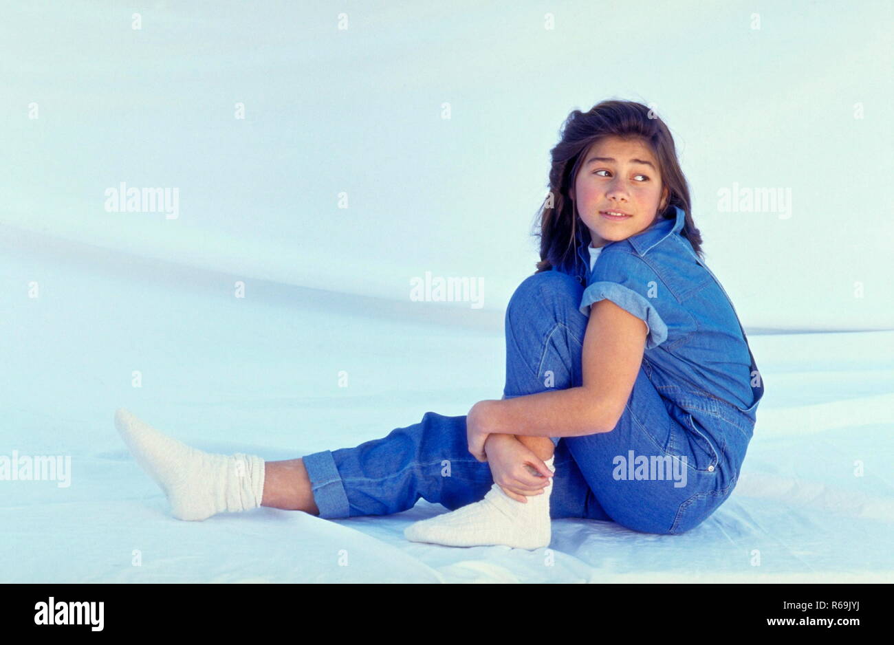 Ritratto, laechelndes Maedchen indianischer Abstammung, 13 Jahre, mit langen schwarzen Haaren mit Jeans und Hemd und weissen Socken, sitzt entspannt auf dem Boden Foto Stock