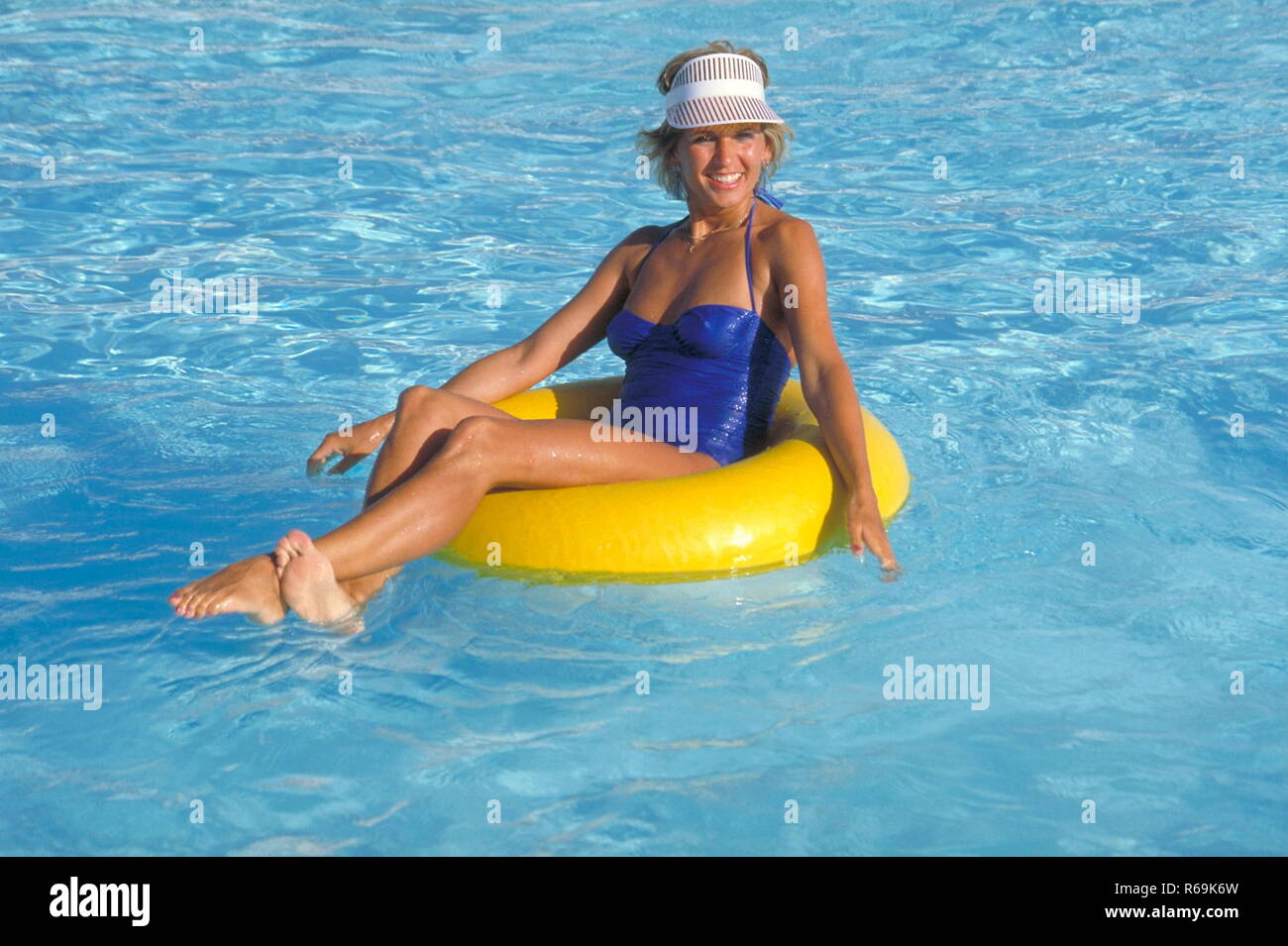 Ritratto, Szene im Freibad, junge Frau mit blauem Badeanzug bekleidet, sitzt in einem gelben Reifen im blauen Wasser des Schwimmbeckens Foto Stock