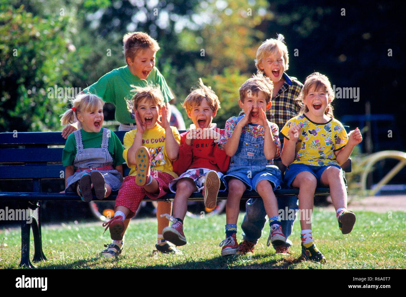 Ritratto, Parkszene, 7 lachende Kinder, 4 bis 10 Jahre alt, sitzen im Sommer auf einer Parkbank Foto Stock