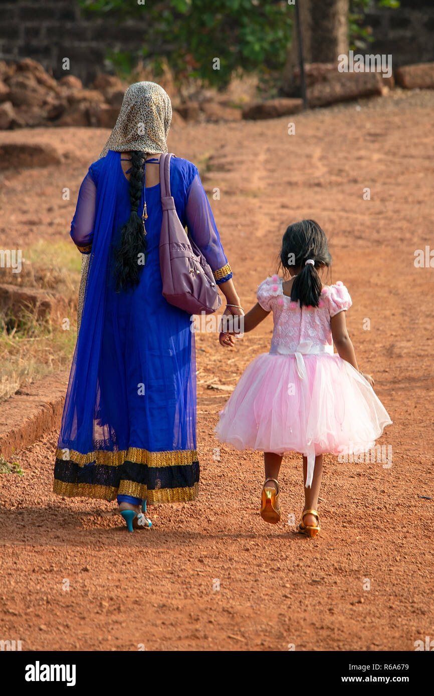 Una donna indiana in un sari colorati passeggiate mano nella mano con la figlia che indossa il suo migliore abito rosa durante una gita di famiglia. Foto Stock