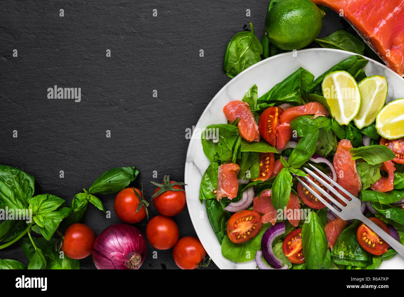 Insalata fresca con salmone, spinaci, pomodori ciliegini, cipolla rossa e basilico in lastra di marmo con la forcella più nero ardesia sfondo. cibo sano concetto. a Foto Stock