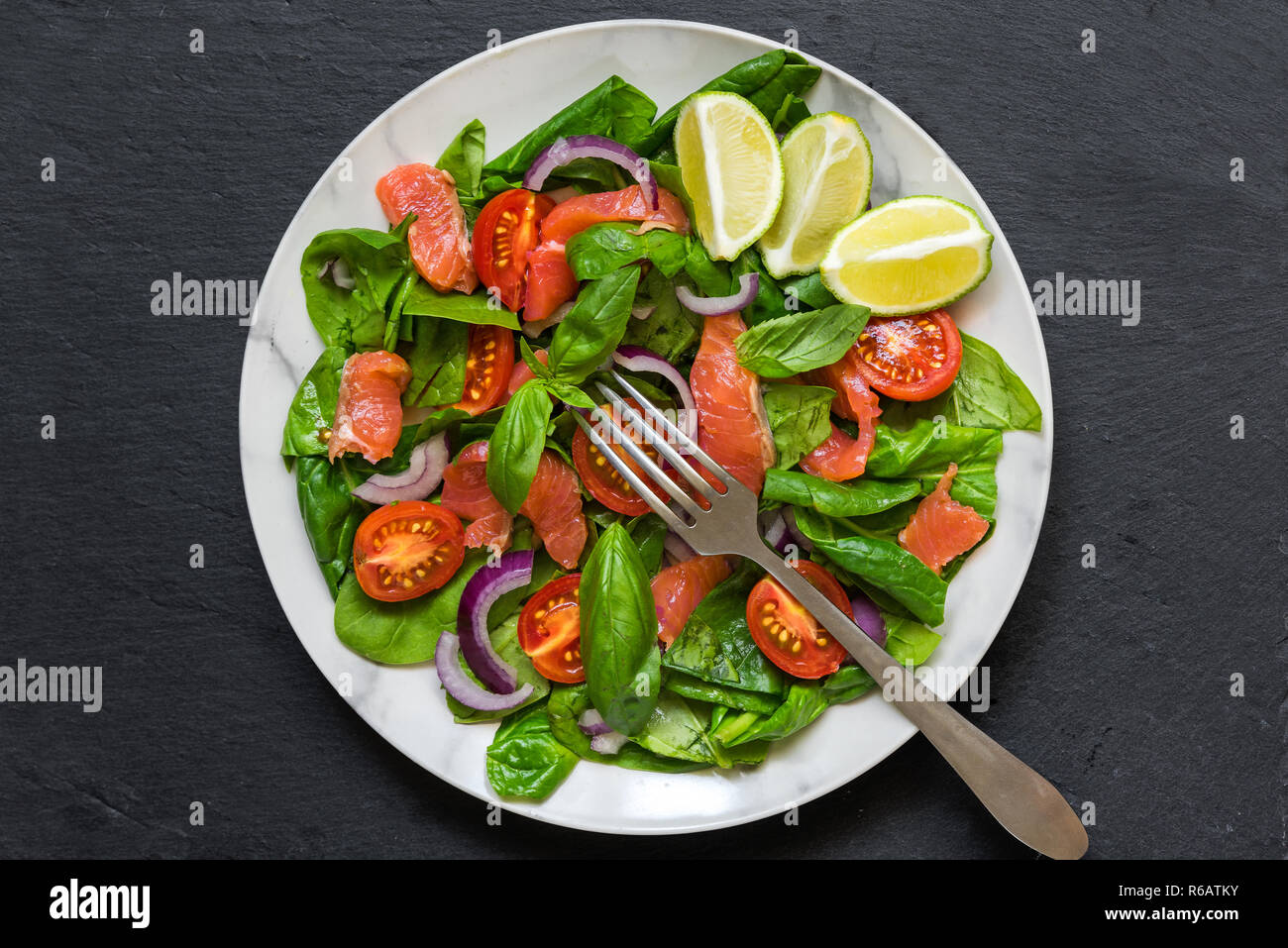 Salmone con insalata di spinaci, pomodori ciliegini, cipolla rossa e basilico con forcella in marmo bianco piastra. cibo sano concetto. vista superiore Foto Stock