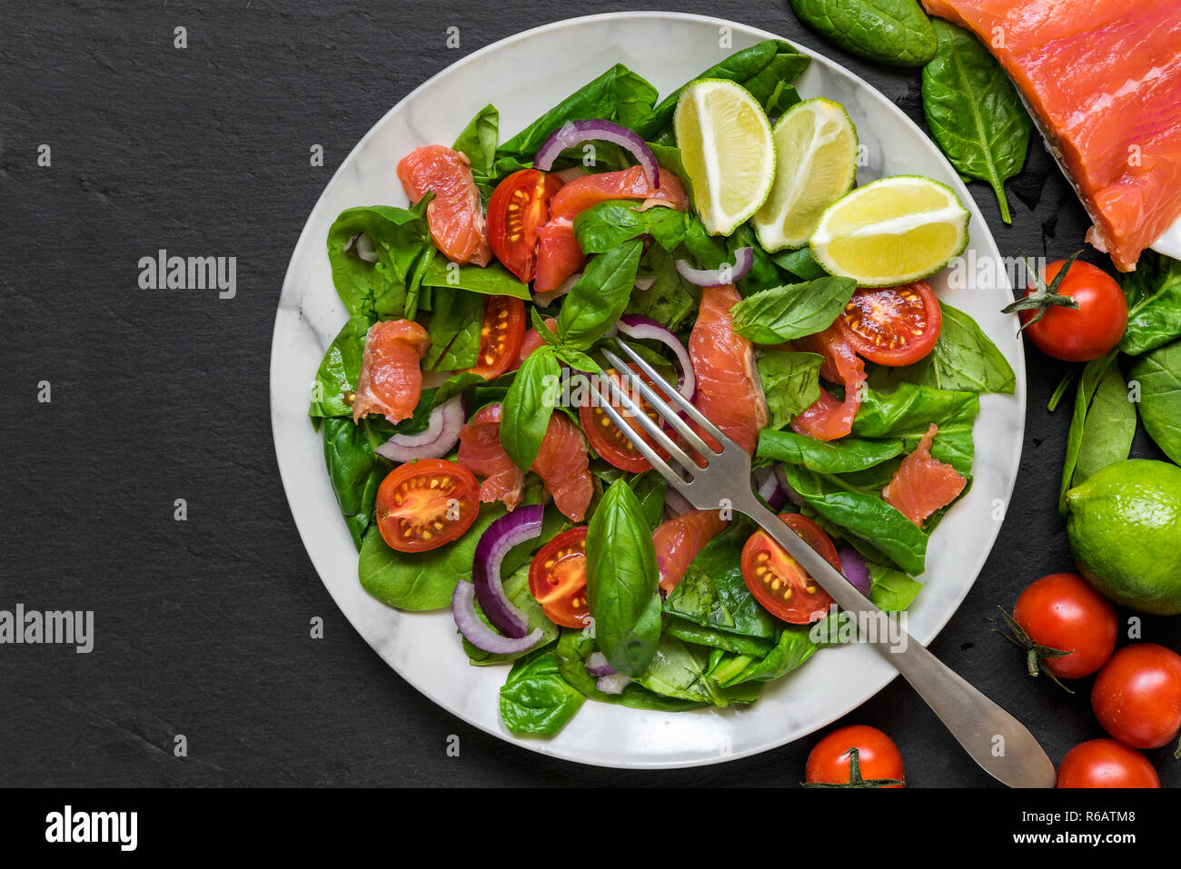 Salmone fresco con insalata di spinaci, pomodori ciliegini, cipolla rossa e basilico in lastra di marmo con la forcella più nero ardesia sfondo. cibo sano concetto. top Foto Stock