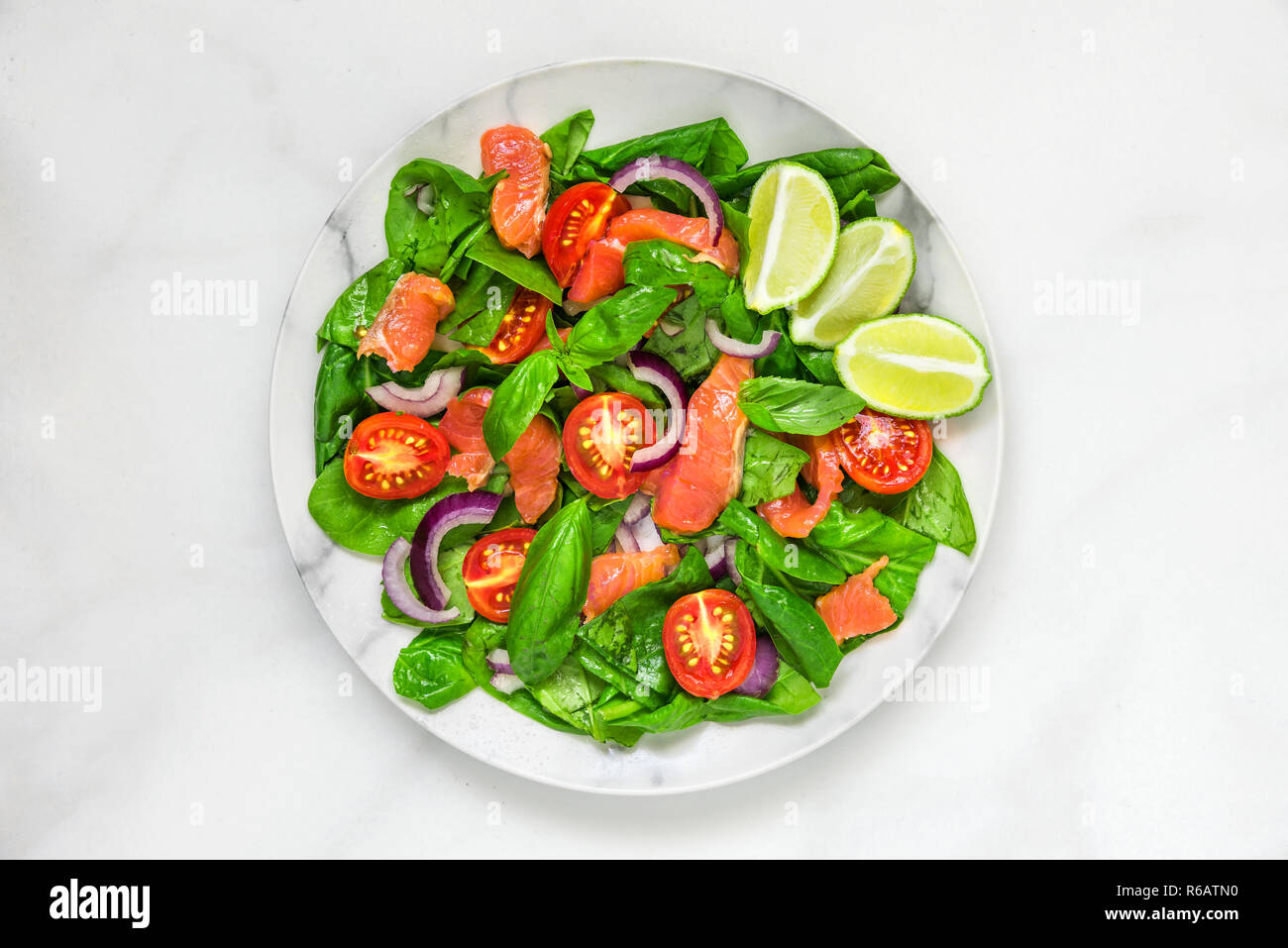 Salmone con insalata di spinaci, pomodori ciliegini, cipolla rossa, succo di limone e foglie di basilico in una lastra di marmo bianco dello sfondo. cibo sano concetto. vista superiore Foto Stock