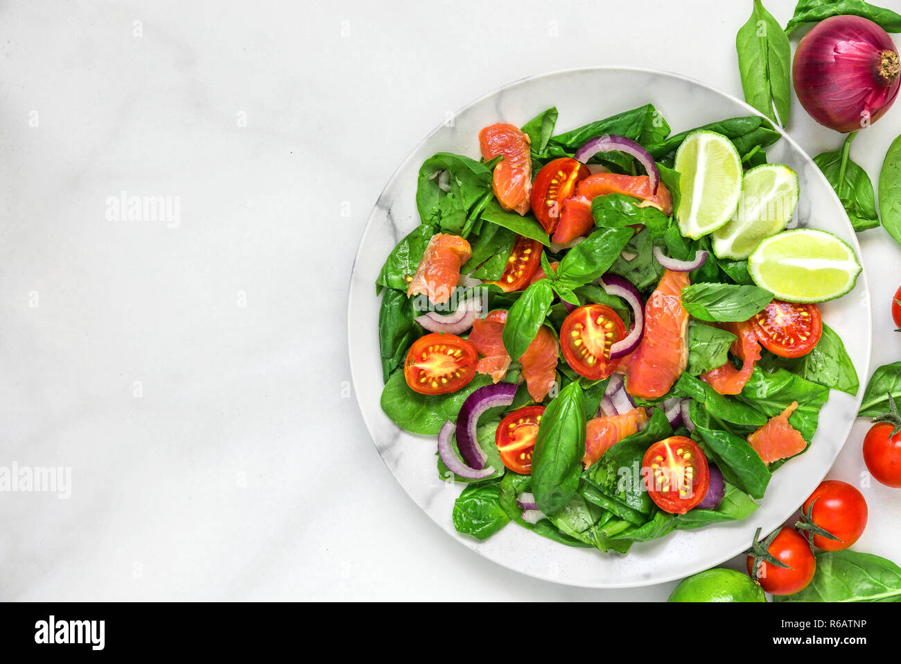 Insalata fresca con salmone, spinaci, pomodori ciliegini, cipolla rossa e basilico in piastra di marmo bianco sulla tavola di marmo. cibo sano concetto. vista superiore con copia Foto Stock