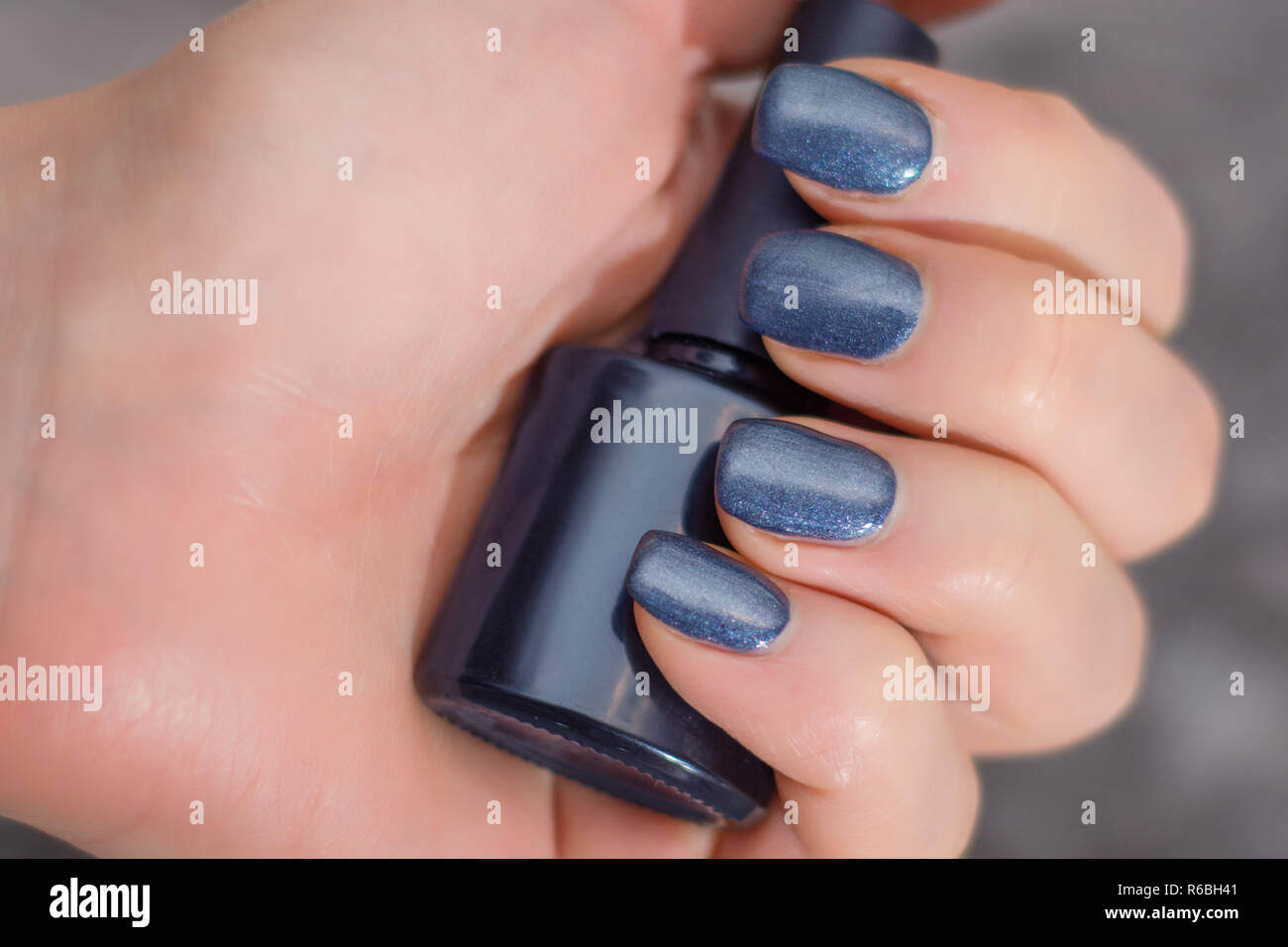 Femmina con mano blu navy manicure sulle dita tenendo la bottiglia per chiodi pittura. Manicure Concetto di immagine. Close up, il fuoco selettivo Foto Stock