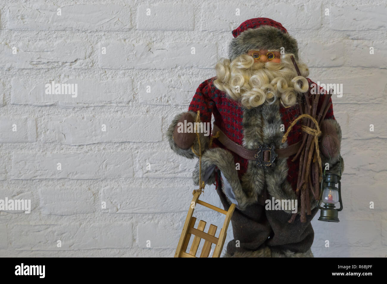 Buon Natale, una santa claus bambola in primo piano tenendo una slitta e lanterna isolato su un bianco muro di mattoni in background Foto Stock