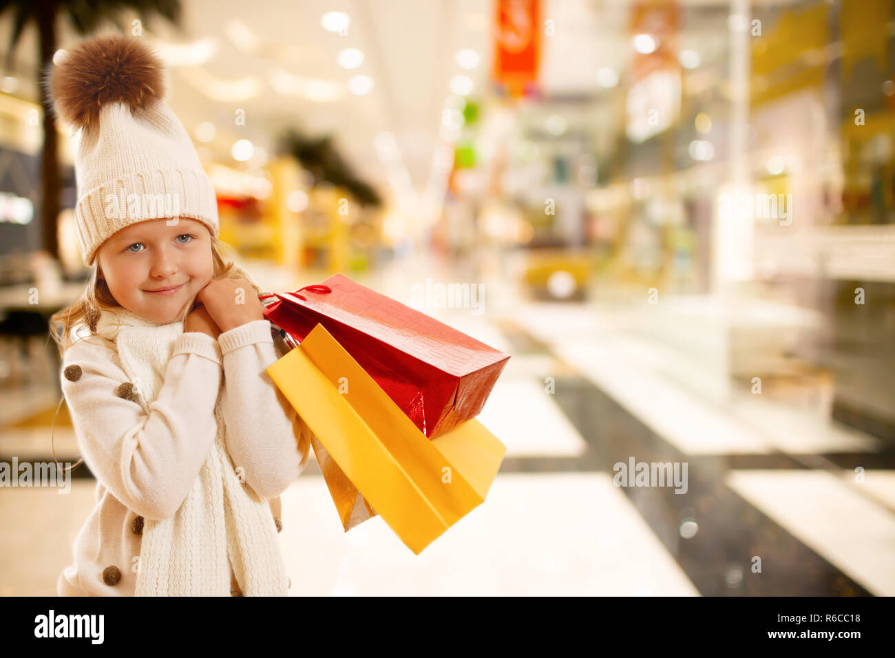 Una ragazzina in un berretto lavorato a maglia con un pompon, sciarpa e un maglione, è in possesso di variopinti sacchetti di carta. Il concetto di acquisti e vendite. In the mall Foto Stock