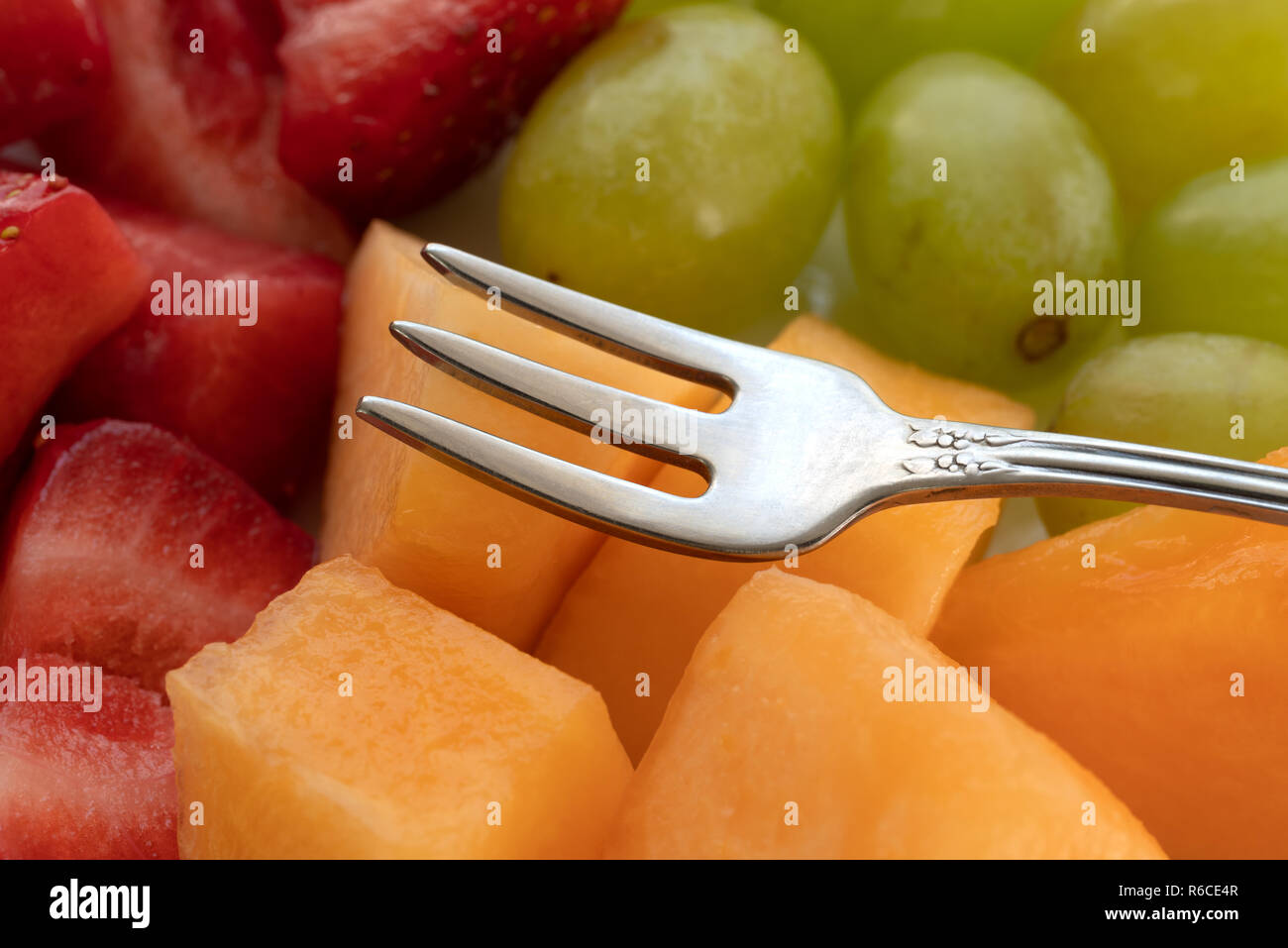 Vista ravvicinata di fragole uva e melone tagliato su una piastra con una piccola forcella di frutta in cima al cibo. Foto Stock