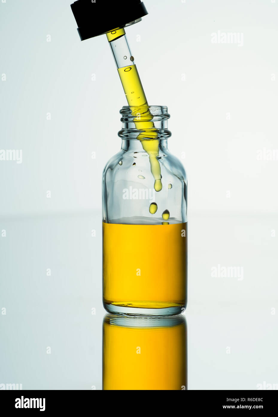 Close up di aprire un vasetto contenente liquido dorato con pipetta di vetro cadere nel liquido Foto Stock
