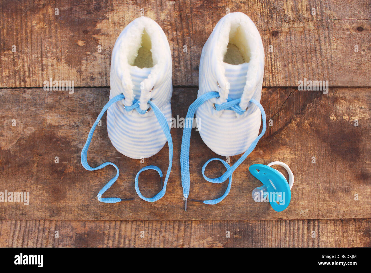 2019 Anno nuovo scritto lacci delle calzature per bambini e ciuccio in legno vecchio sfondo. Vista dall'alto. Lay piatto. Tonica immagine. Foto Stock