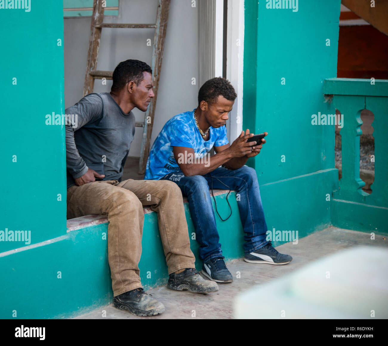 Due uomini cubano guardando un telefono cellulare durante una pausa nella loro giornata lavorativa. Foto Stock