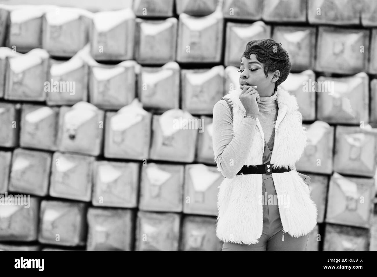 African American donna in pantaloni rosso e bianco pelliccia giacca poste a giornata invernale contro la pietra innevate sullo sfondo. Foto Stock