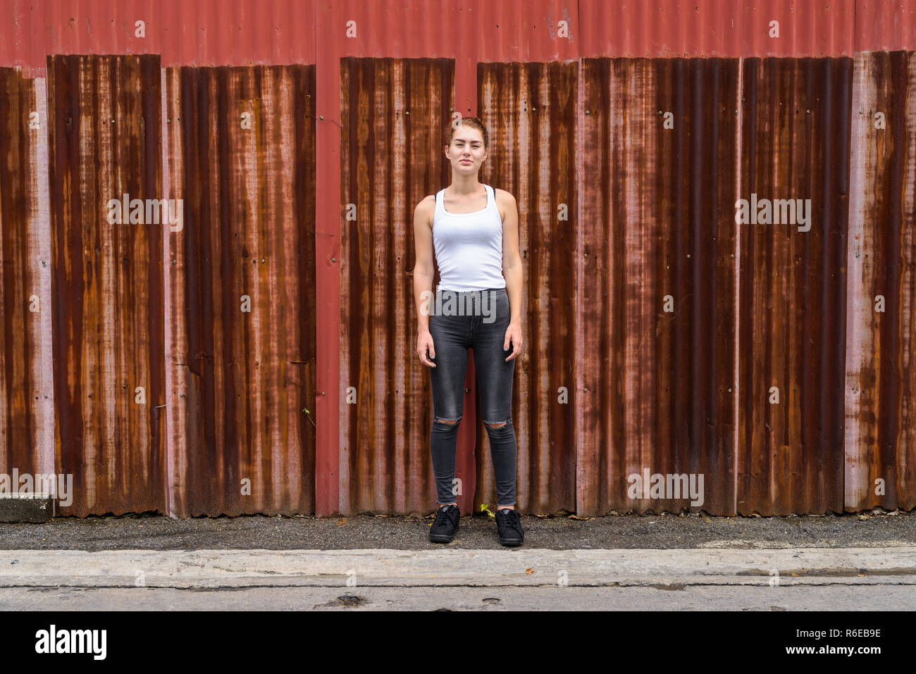 Giovane bella ragazza adolescente in piedi contro il vecchio foglio arrugginito wa Foto Stock