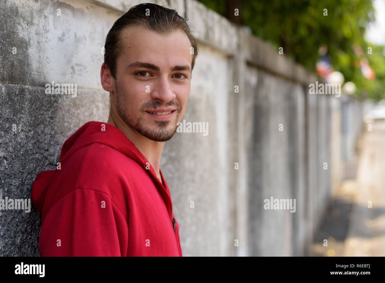 Felice giovane uomo barbuto sorridere mentre indossa felpa con cappuccio rosso e lea Foto Stock