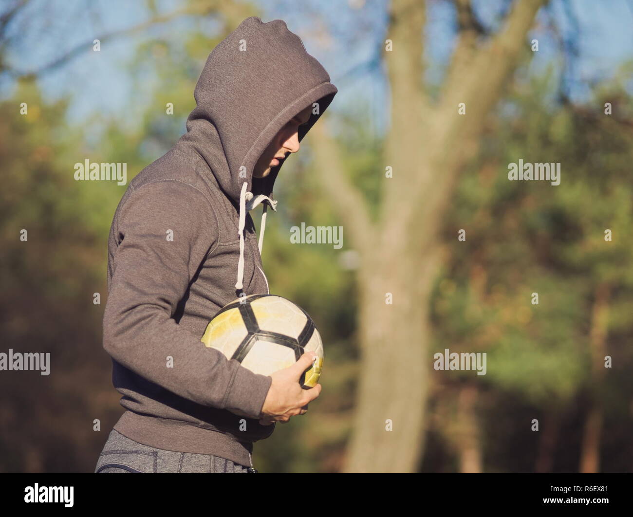 Giocatore di calcio in posa con il calcio nel parco su una soleggiata giornata autunnale Foto Stock