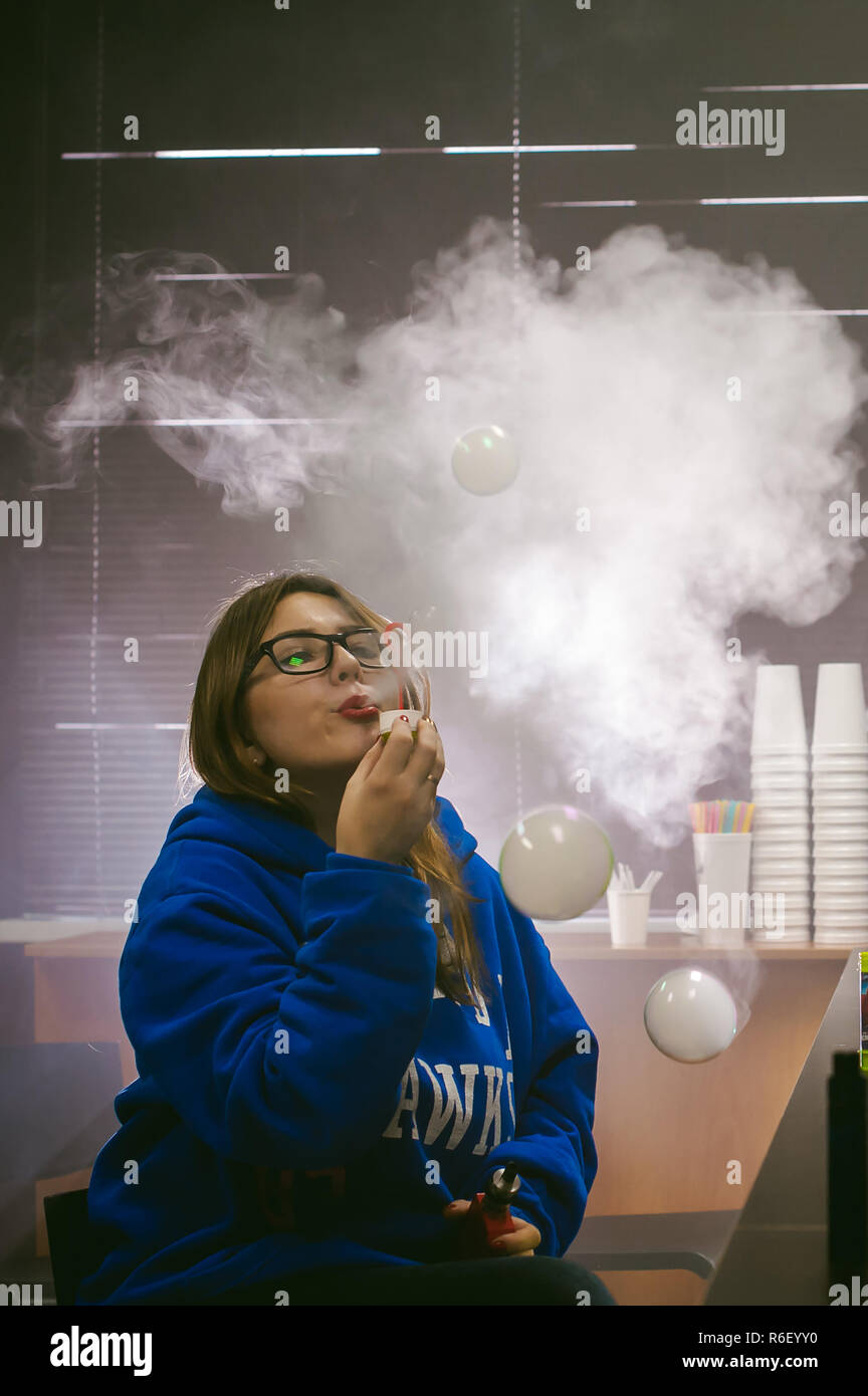 Giovane donna carina, il venditore in vape shop shop, il fumo di sigaretta  elettronica, vaping e rilascia una nuvola di vapore e gonfia bolle di  sapone Foto stock
