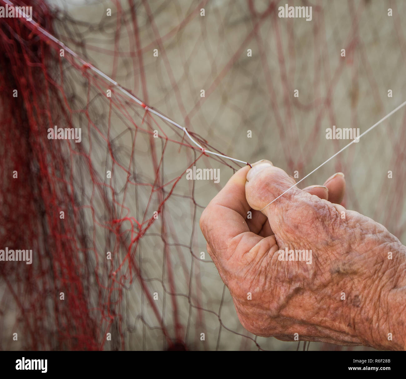 La mano di un vecchio pescatore riparando le reti per la pesca Foto Stock