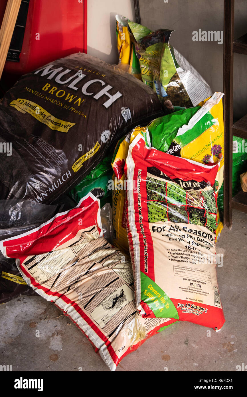 Sacchetti di strame, fertilizzante e alghe killer per tappeti erbosi impilati in un garage. Kansas, Stati Uniti d'America. Foto Stock
