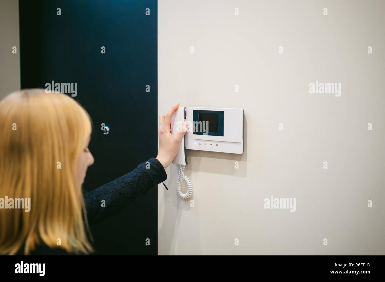 Donna bionda riaggancia il telefono dopo aver risposto a una chiamata interna nel suo appartamento Foto Stock