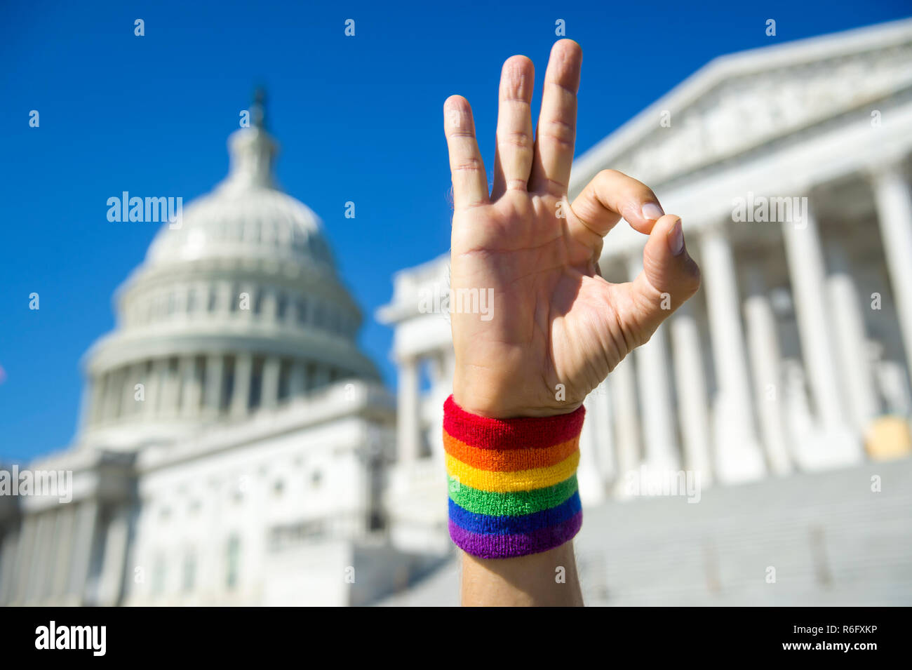Mano che indossa il Gay Pride rainbow con la fascetta da polso rendendo okay gesto di fronte al Campidoglio di Washington DC, Stati Uniti d'America Foto Stock