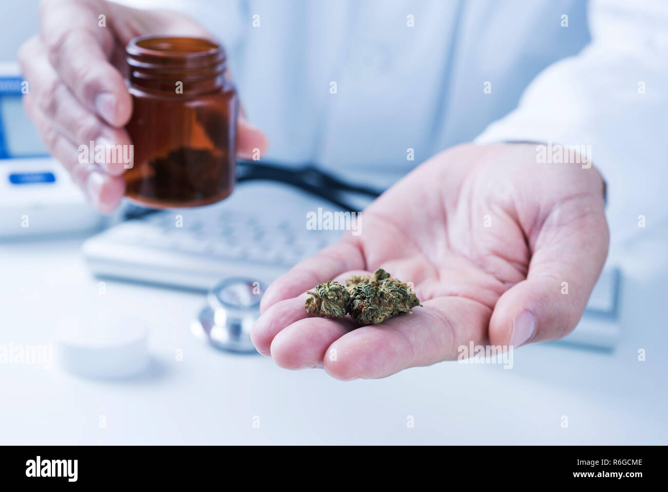 Primo piano di un medico caucasica uomo in camice bianco, seduto alla sua scrivania, con alcune gemme di marijuana in mano Foto Stock