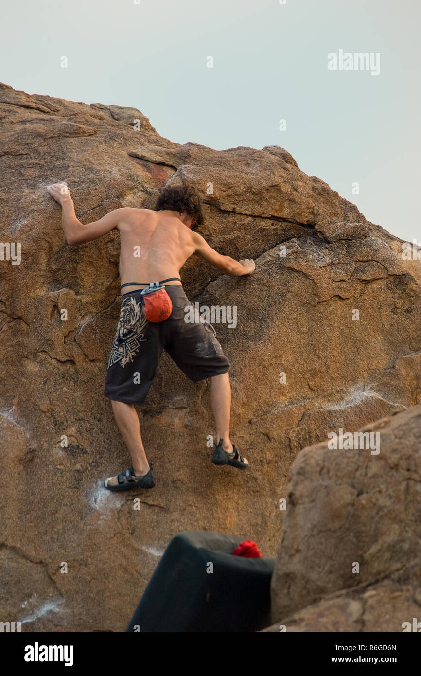 Un maschio di rocciatore pratiche le sue abilità, la presa e la forza arrampicata boulder con un tappetino di crash al di sotto di lui per la sicurezza. Foto Stock