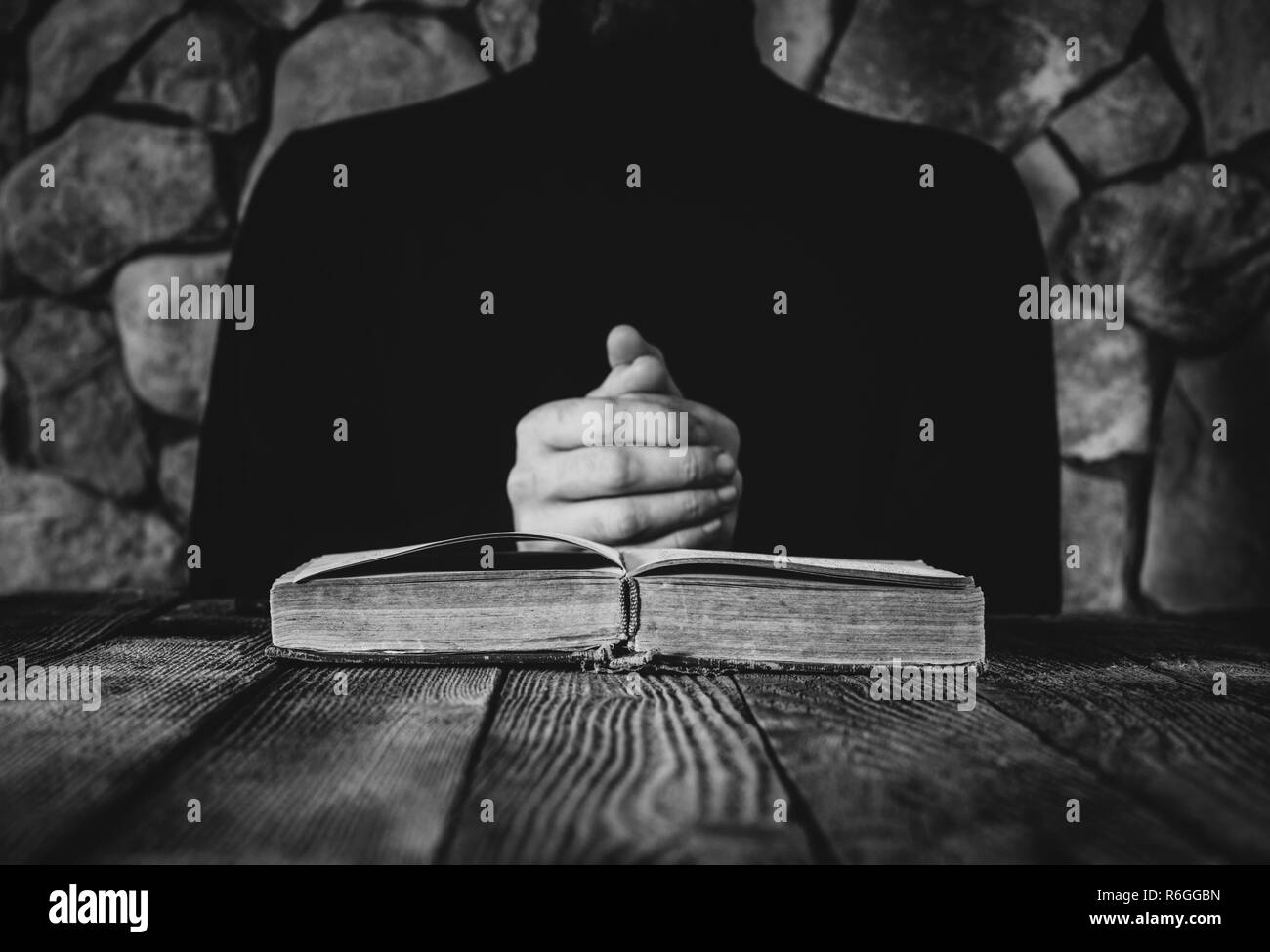 Maschio di vestiti di nero nella parte anteriore di un vecchio libro aperto. il concetto di preghiera, studio, stregoneria. Il fuoco selettivo in bianco nero photo Foto Stock