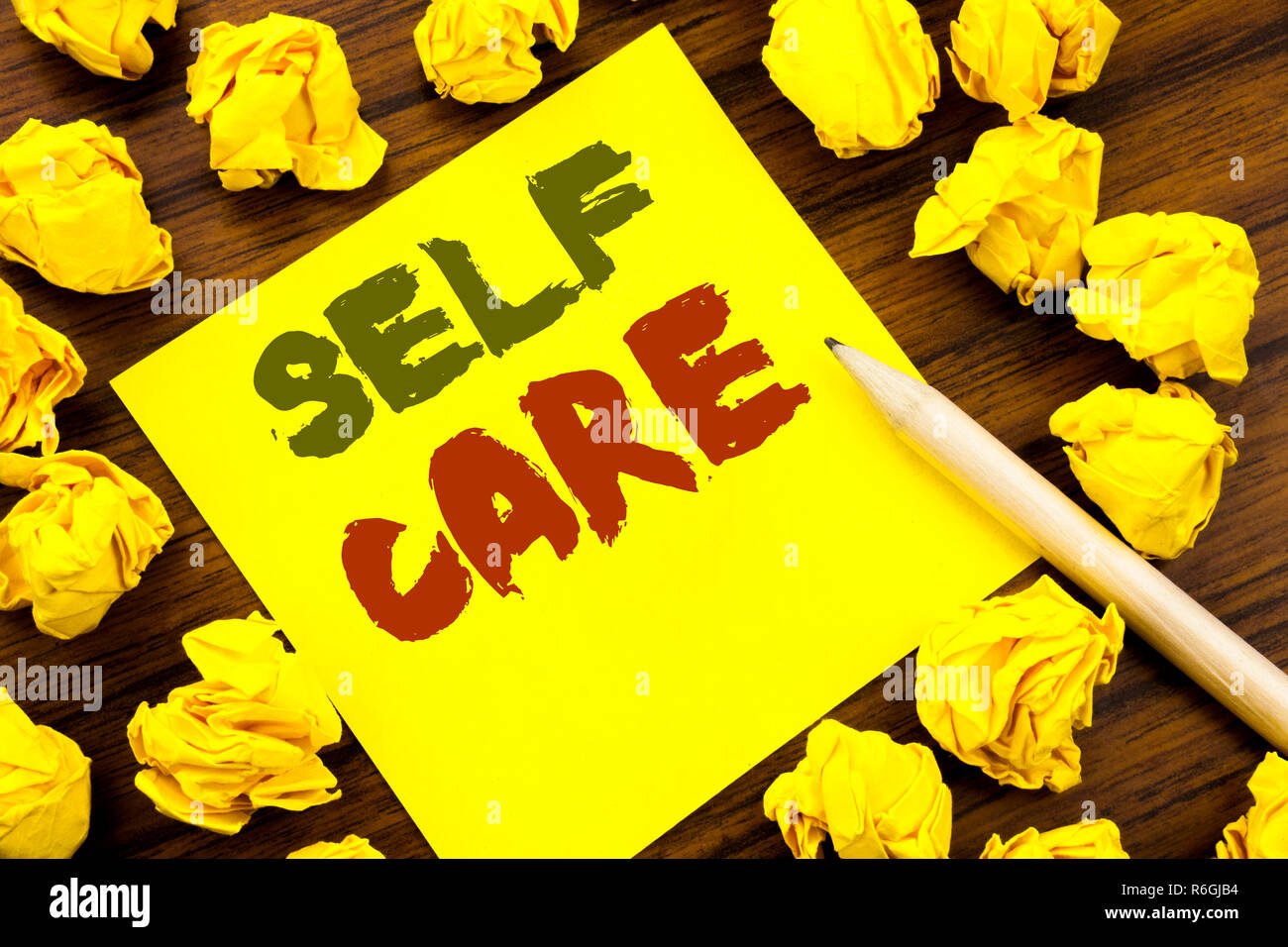 La parola, la scrittura Self Care. Il concetto di business per prendere la cura per la propria salute scritto su una nota adesiva carta, legno con sfondo giallo piegata la carta nel senso di pensare Foto Stock