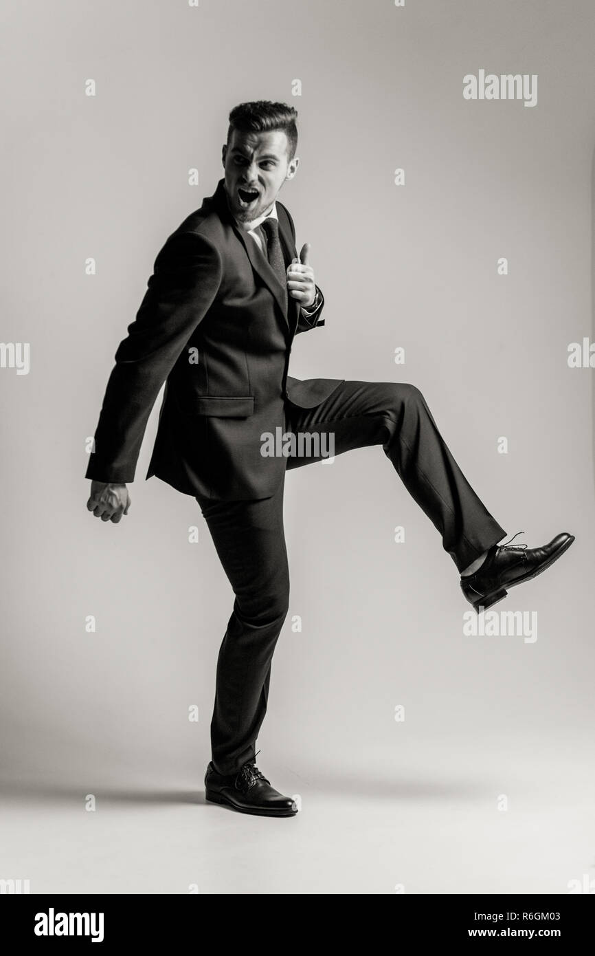 Angry Young Imprenditore in un abito nero e una camicia bianca è urlando in  furia e calci con rabbia. Immagine in bianco e nero Foto stock - Alamy