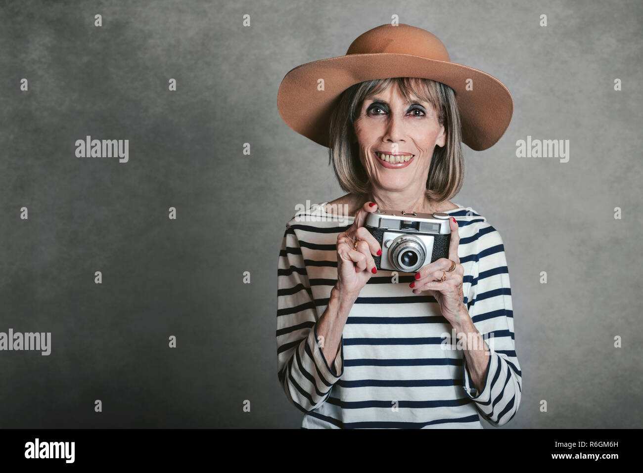 Ritratto di sorridente donna senior con foto vintage fotocamera su sfondo grigio Foto Stock