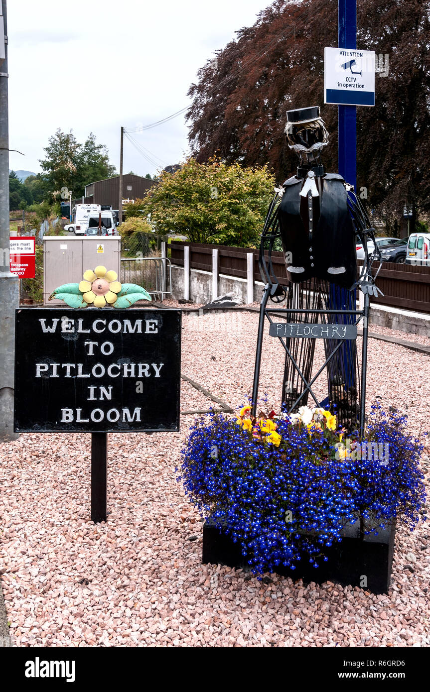 Un eccentrico la figura di una ferrovia porter abilmente scolpiti da vergelle spingendo una mano carrello portante una varietà di coloratissimi fiori Foto Stock